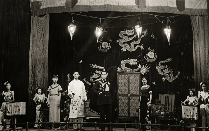 舞台照:深色帷幕与双龙布景,四盏吊灯下一排演员分立道具两侧