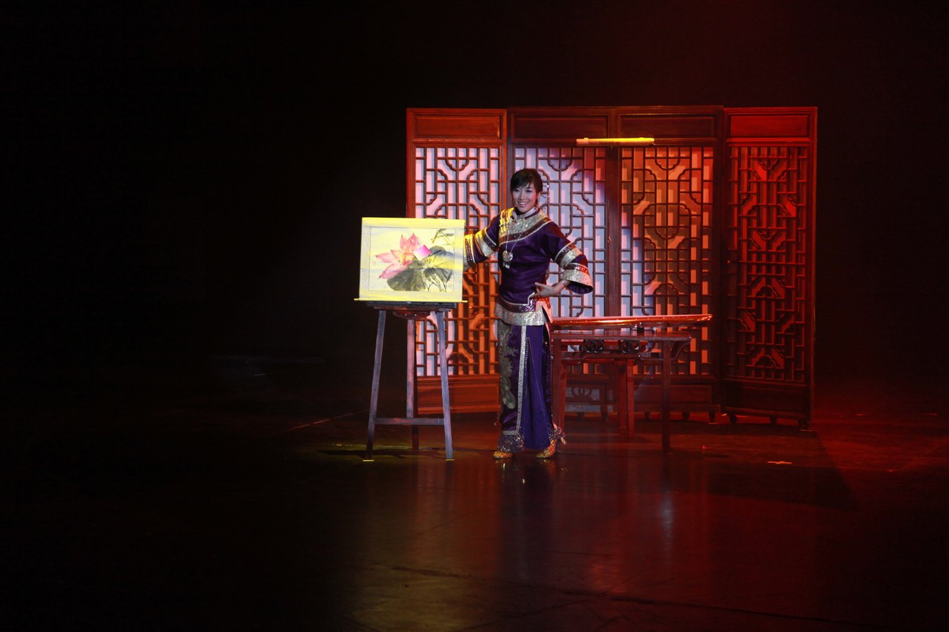 刘蓓在红色屏风布景前演出《秀色》,身旁画架上立着一幅荷花