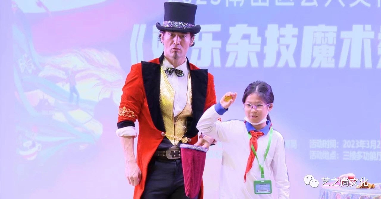 他身着红色礼服与礼帽,身旁站着一位系红领巾的学生,身后是活动背板